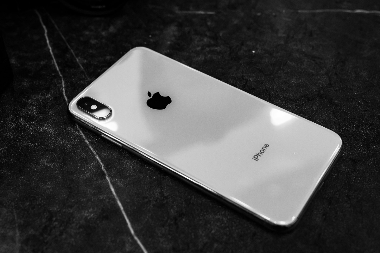 Black and white photo of a sleek smartphone resting on a dark marble surface, showcasing elegance and design.